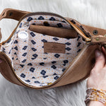Brown leather bag with floral interior, held open by hands on a white background