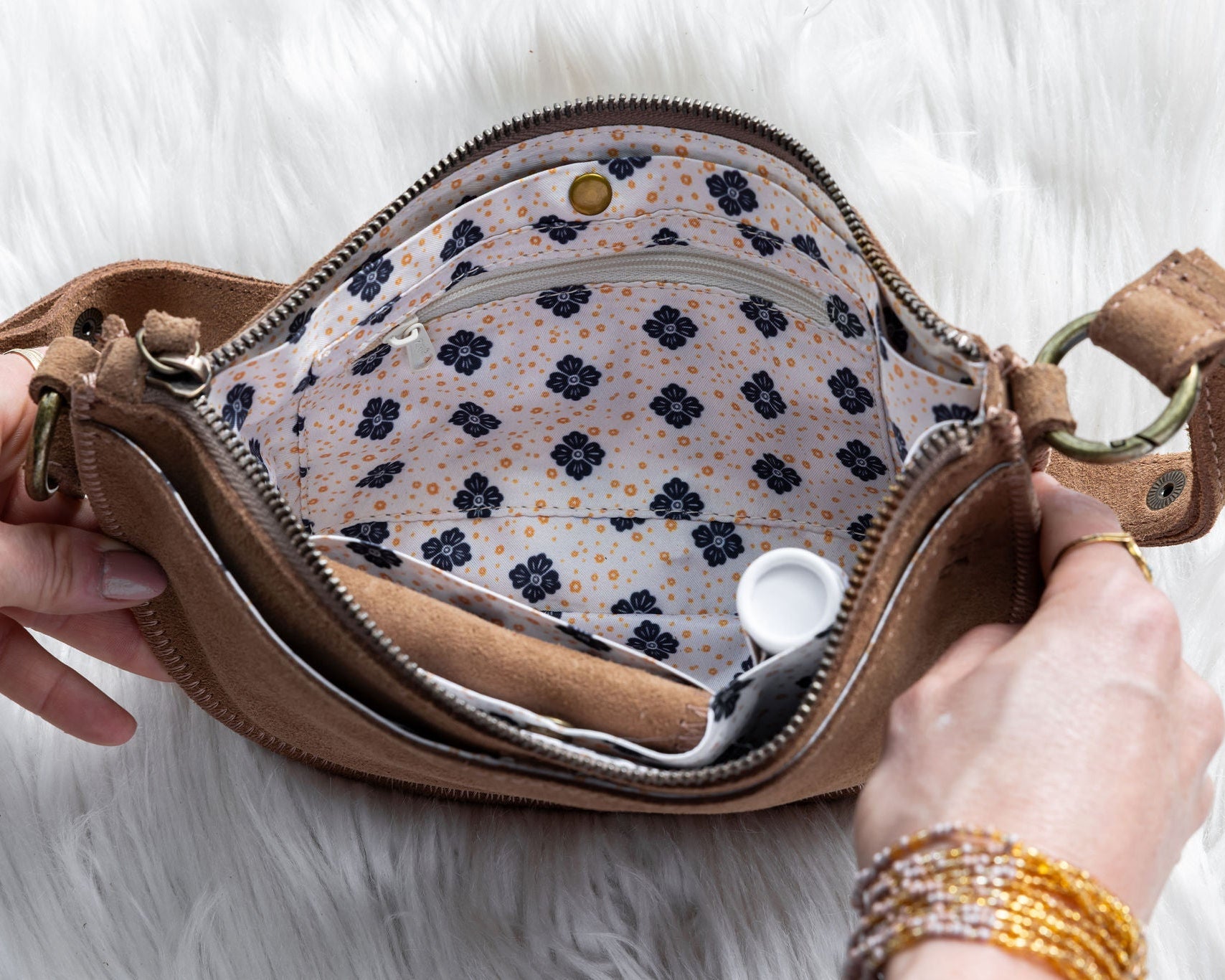 Brown leather bag with floral interior held open by hands on a light background
