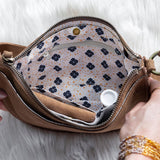 Brown leather bag with floral interior held open by hands on a light background
