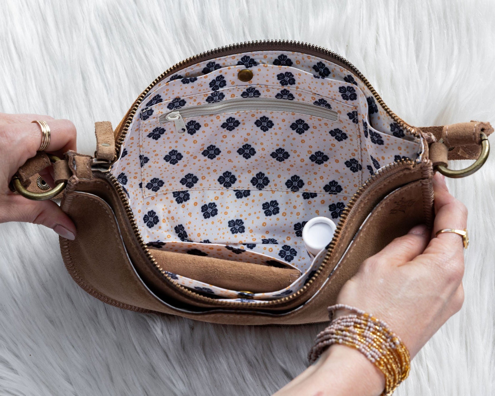 Person opening a brown leather clutch with floral interior on a white fur surface