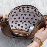 Person opening a brown leather clutch with floral interior on a white fur surface