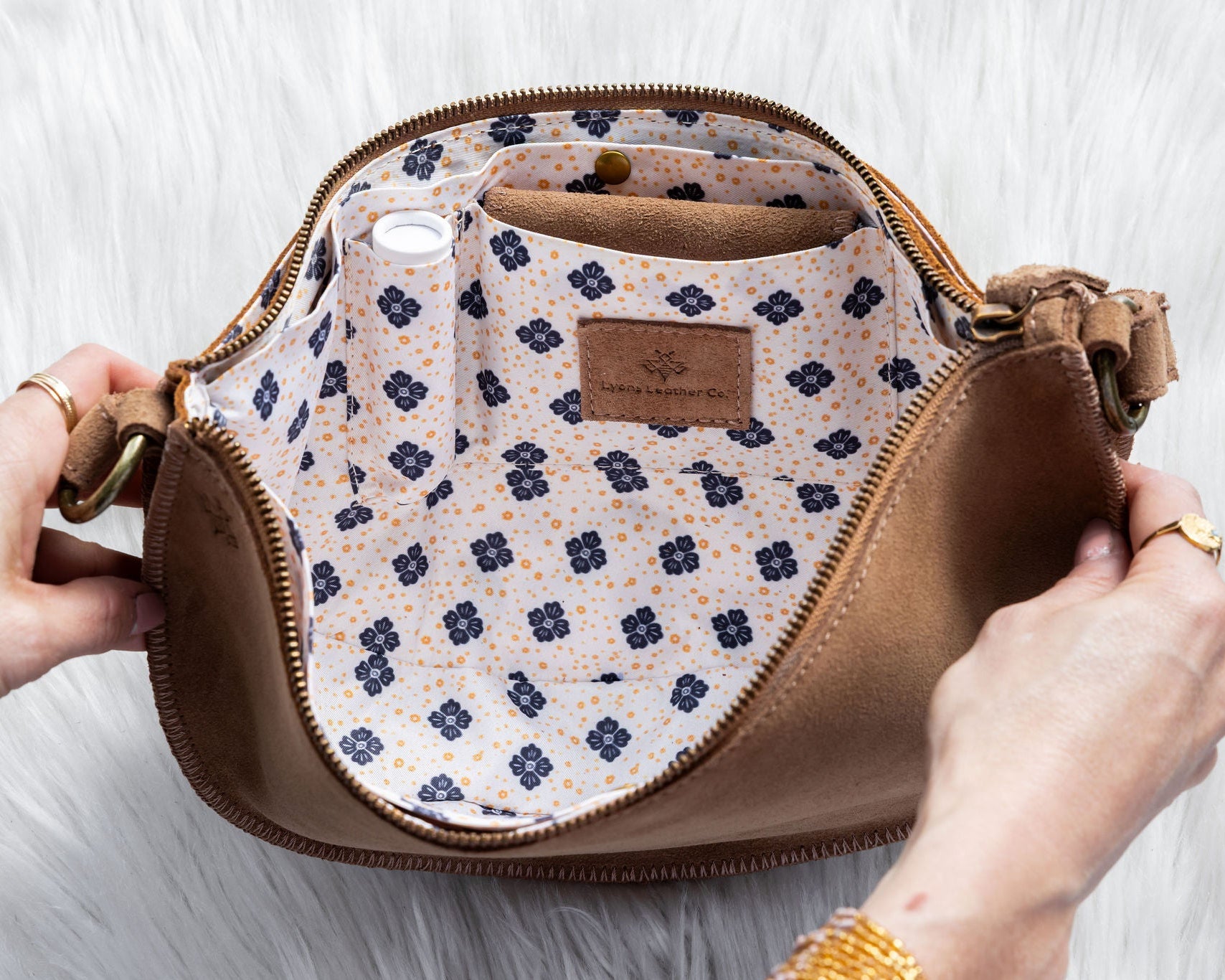 Brown handbag with floral interior pocket held by a person on a white background