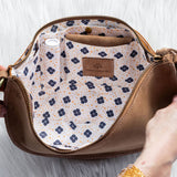 Brown handbag with floral interior pocket held by a person on a white background