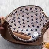 Brown leather bag with floral interior being held open by a person on a light gray background
