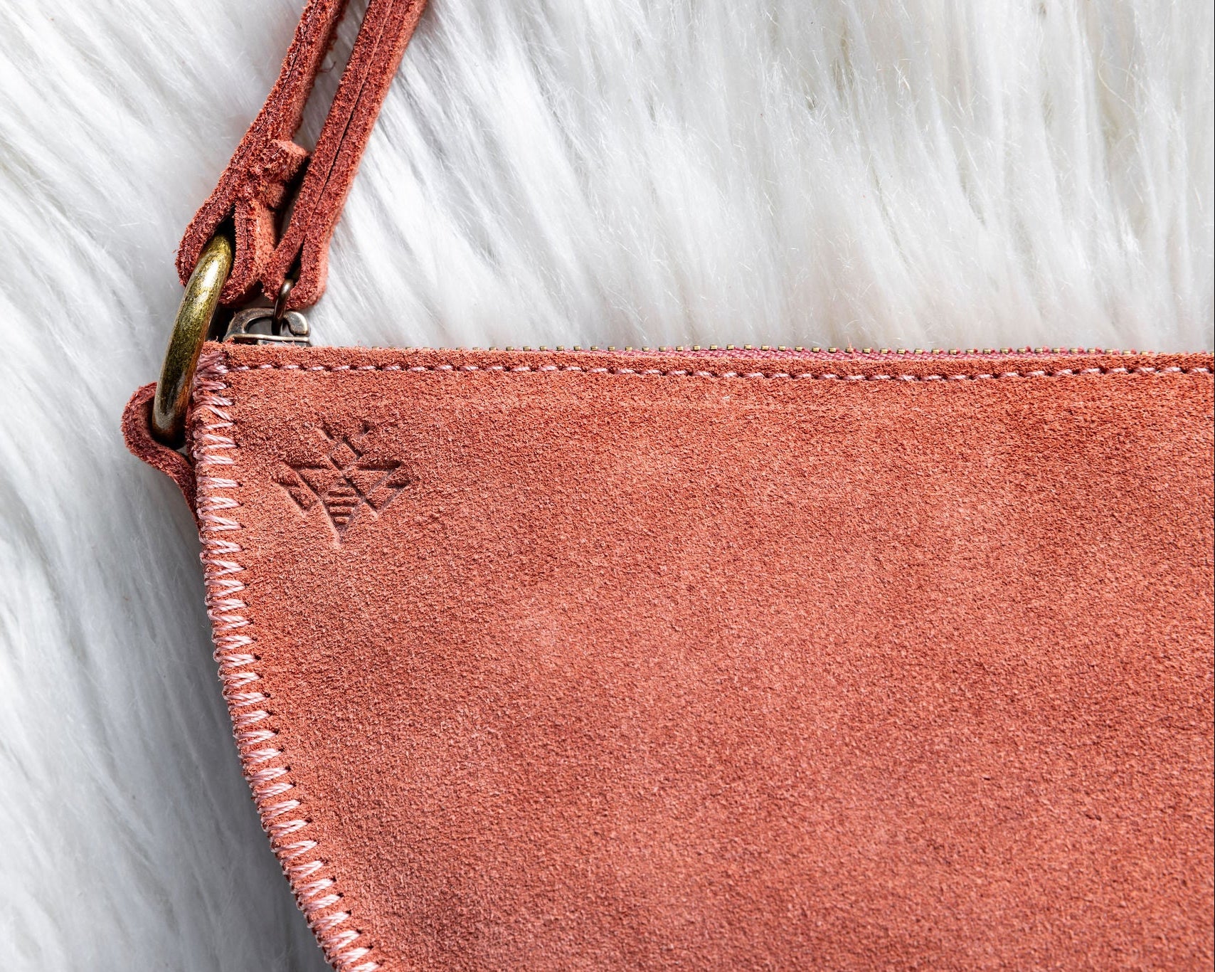 Close-up of a pink suede handbag with a red strap on a white fur background