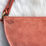 Close-up of a pink suede handbag with a red strap on a white fur background