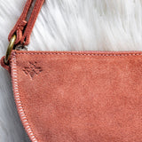 Close-up of a pink suede handbag with a red strap on a white fur background