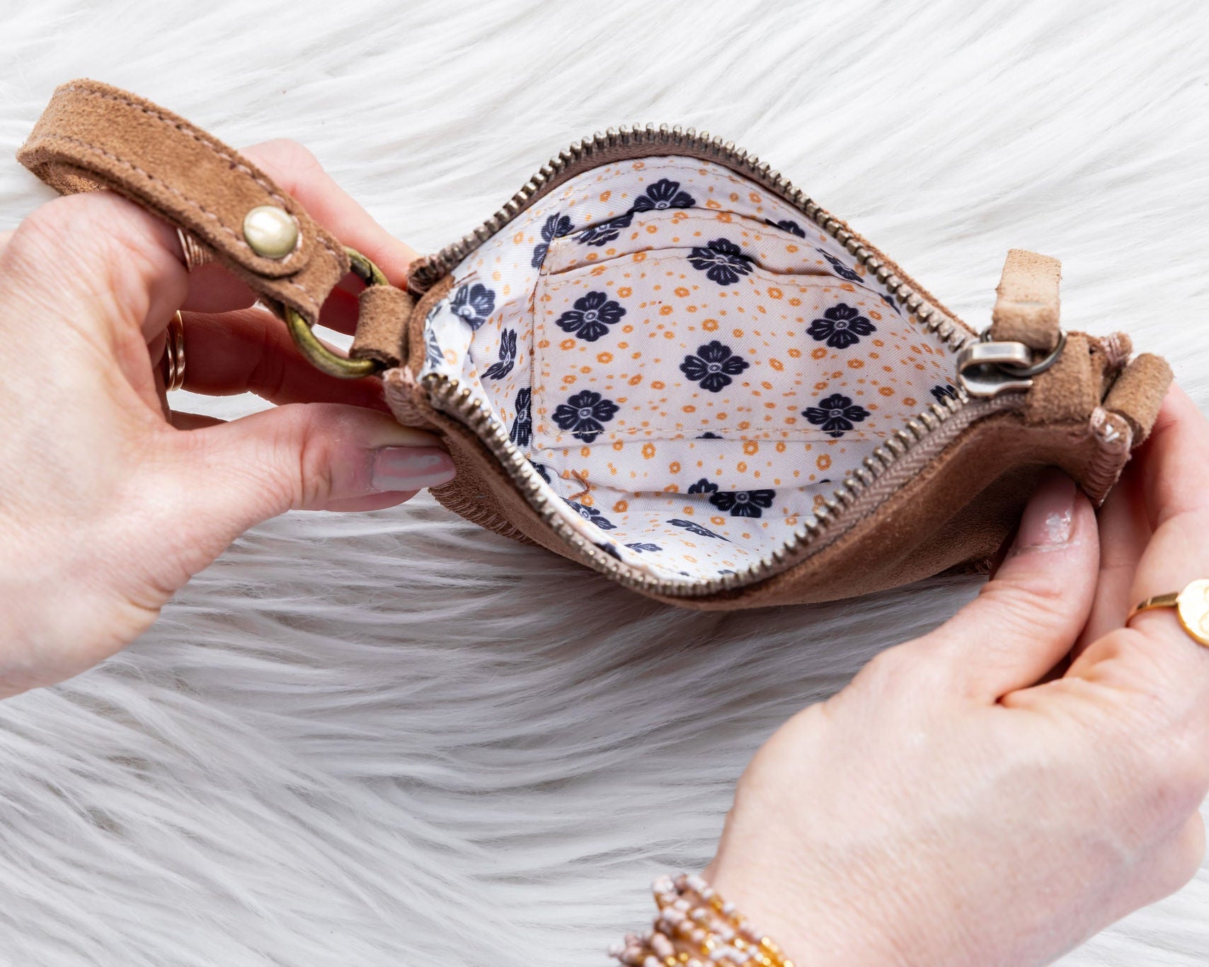 Person holding a small brown leather pouch with floral interior on a white background