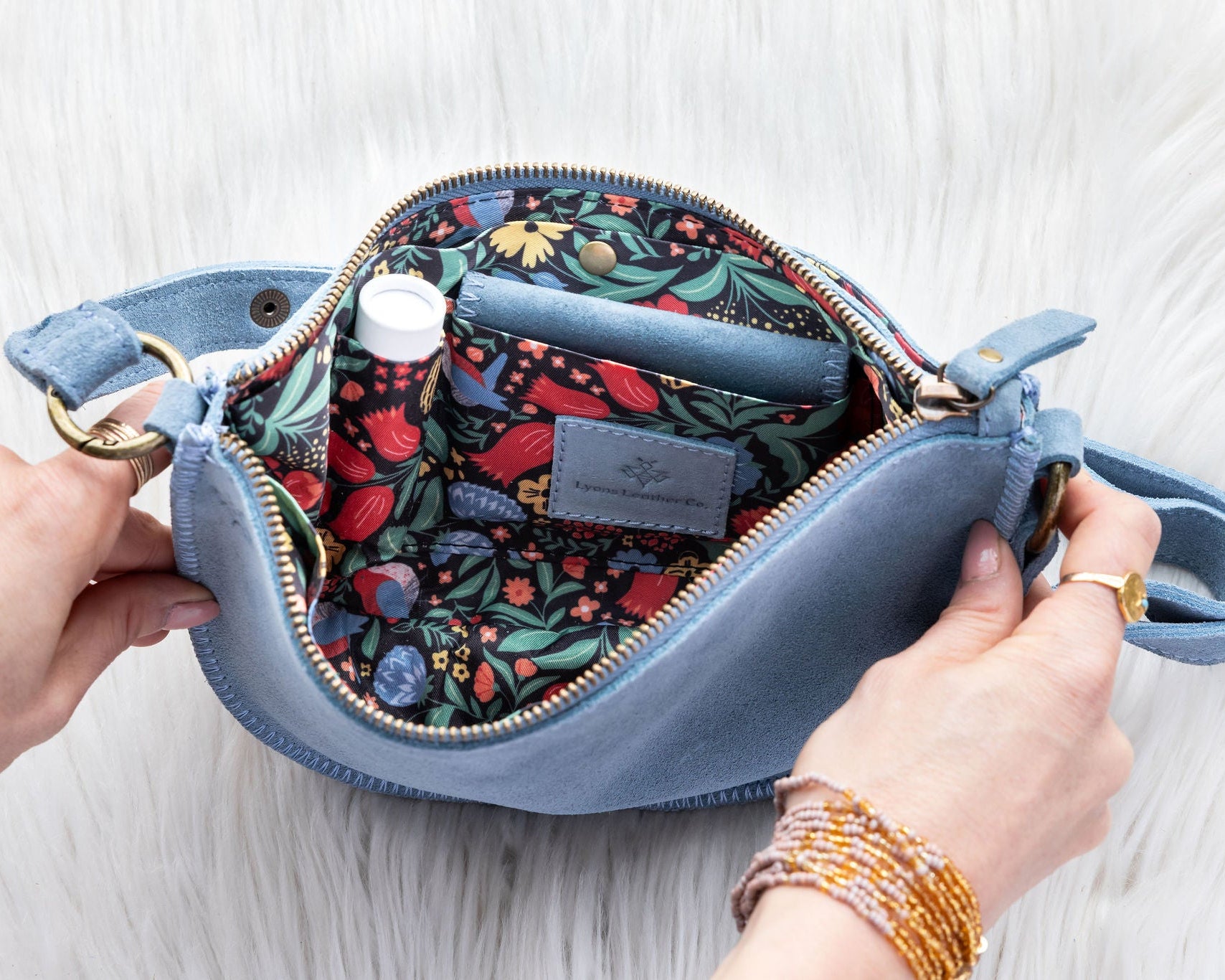 Blue handbag with floral interior, held open by hands on a light background