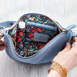 Blue handbag with floral interior, held open by hands on a light background