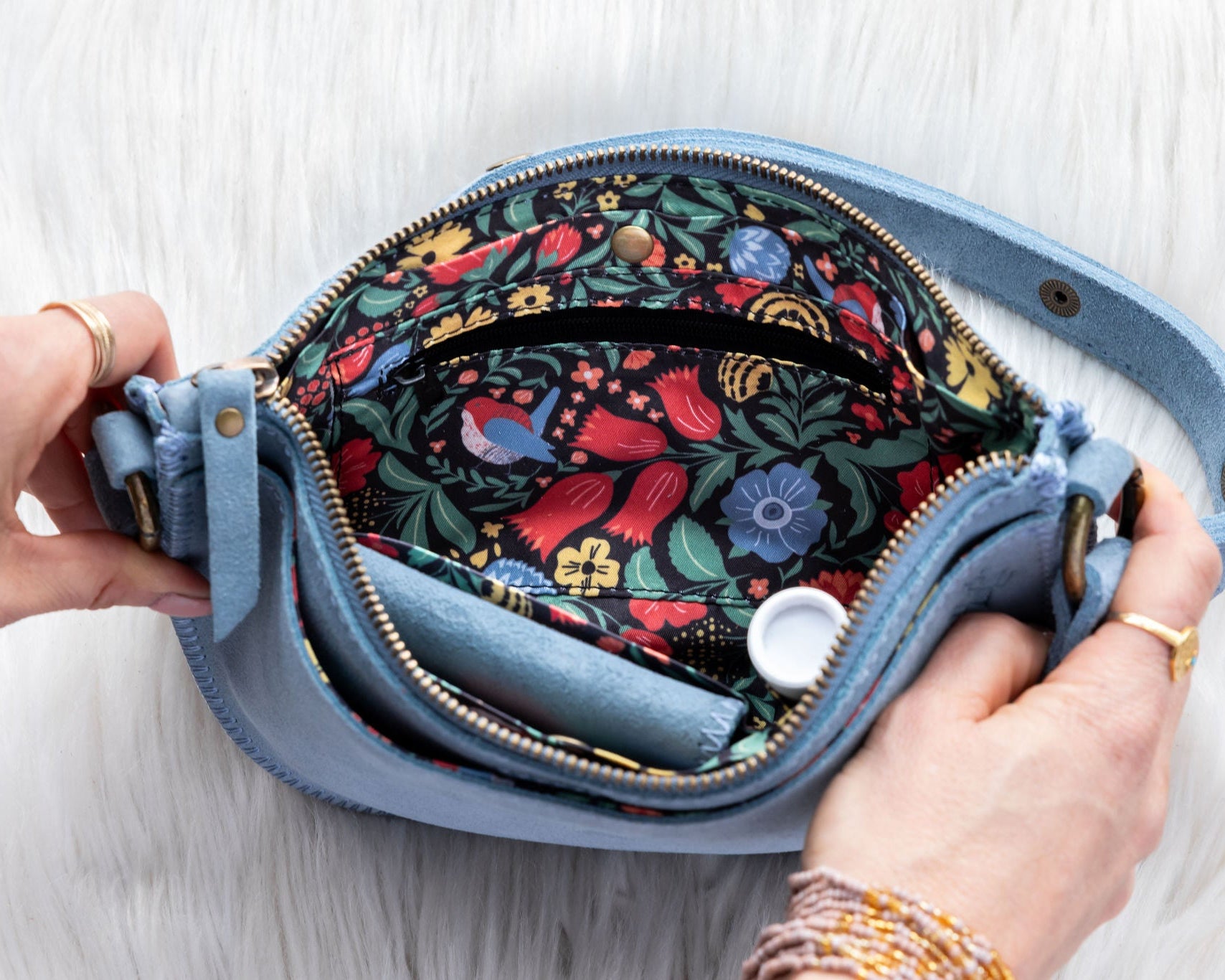 Blue handbag with floral interior held open by a hand on a light wooden surface