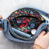 Blue handbag with floral interior held open by a hand on a light wooden surface