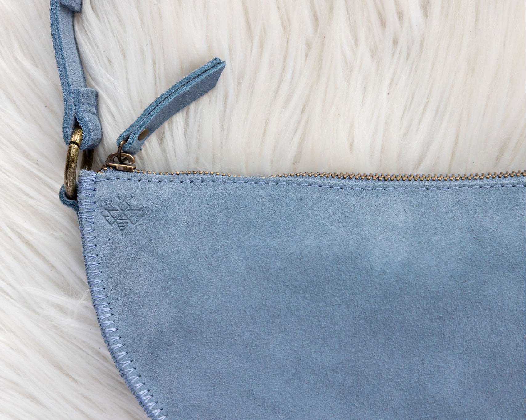 Close-up of a blue suede handbag with a gold zipper on a textured beige surface