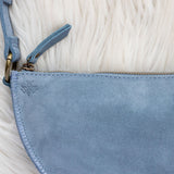 Close-up of a blue suede handbag with a gold zipper on a textured beige surface
