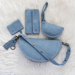 Set of blue leather bags including a handbag, wallet, and cardholder on a white fur background.