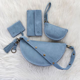 Set of blue leather bags including a handbag, wallet, and cardholder on a white fur background.