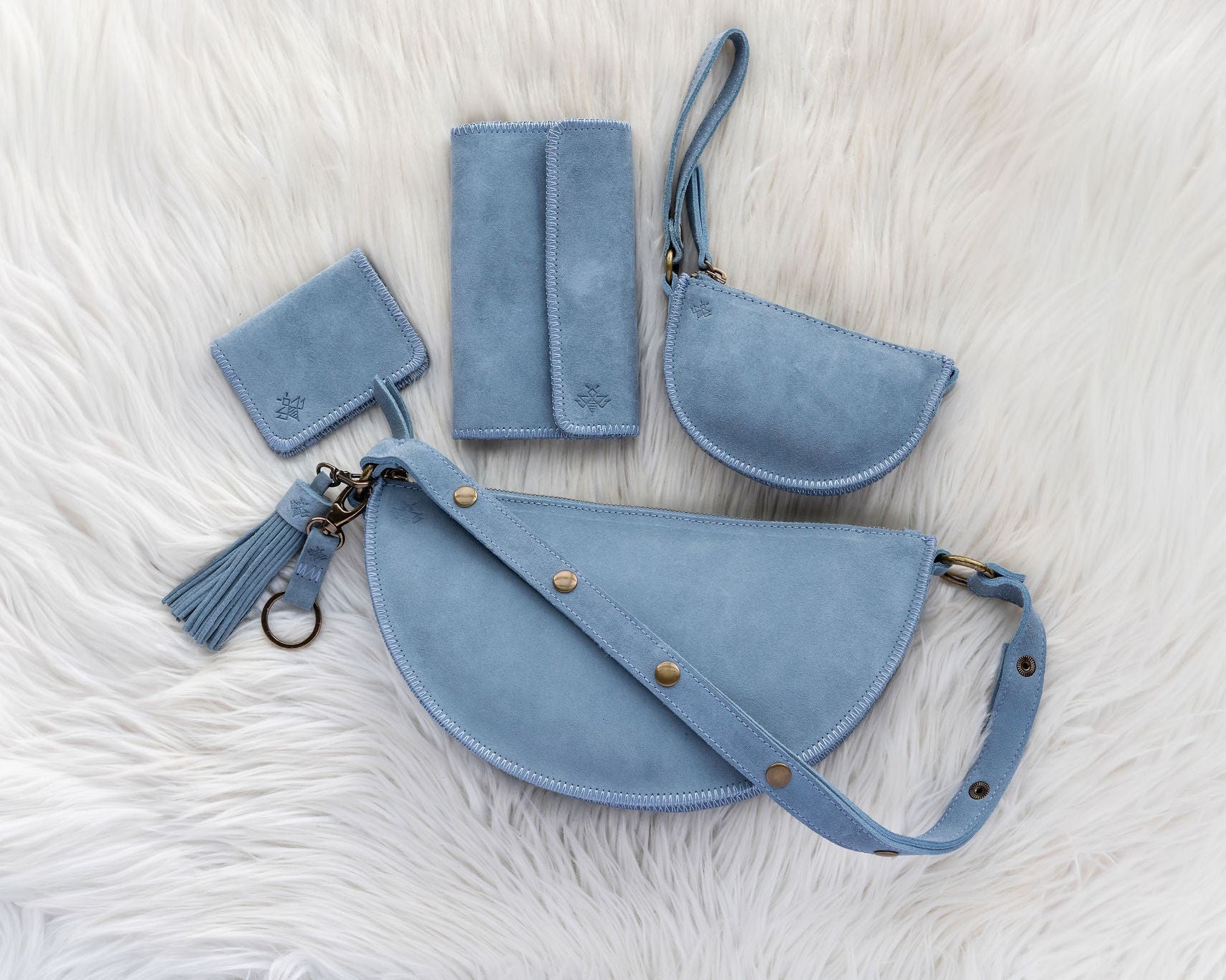 Set of blue leather bags including a handbag, wallet, and cardholder on a white fur background.