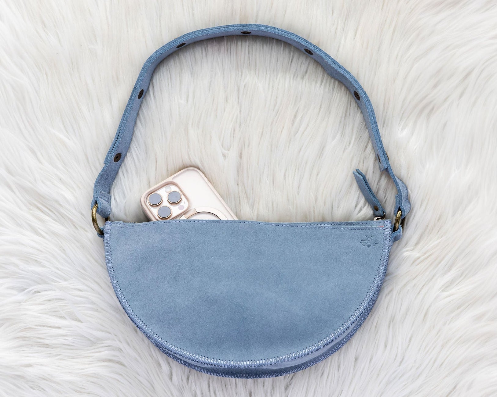 Blue suede handbag with a phone inside on a white fur surface