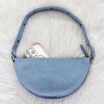 Blue suede handbag with a phone inside on a white fur surface