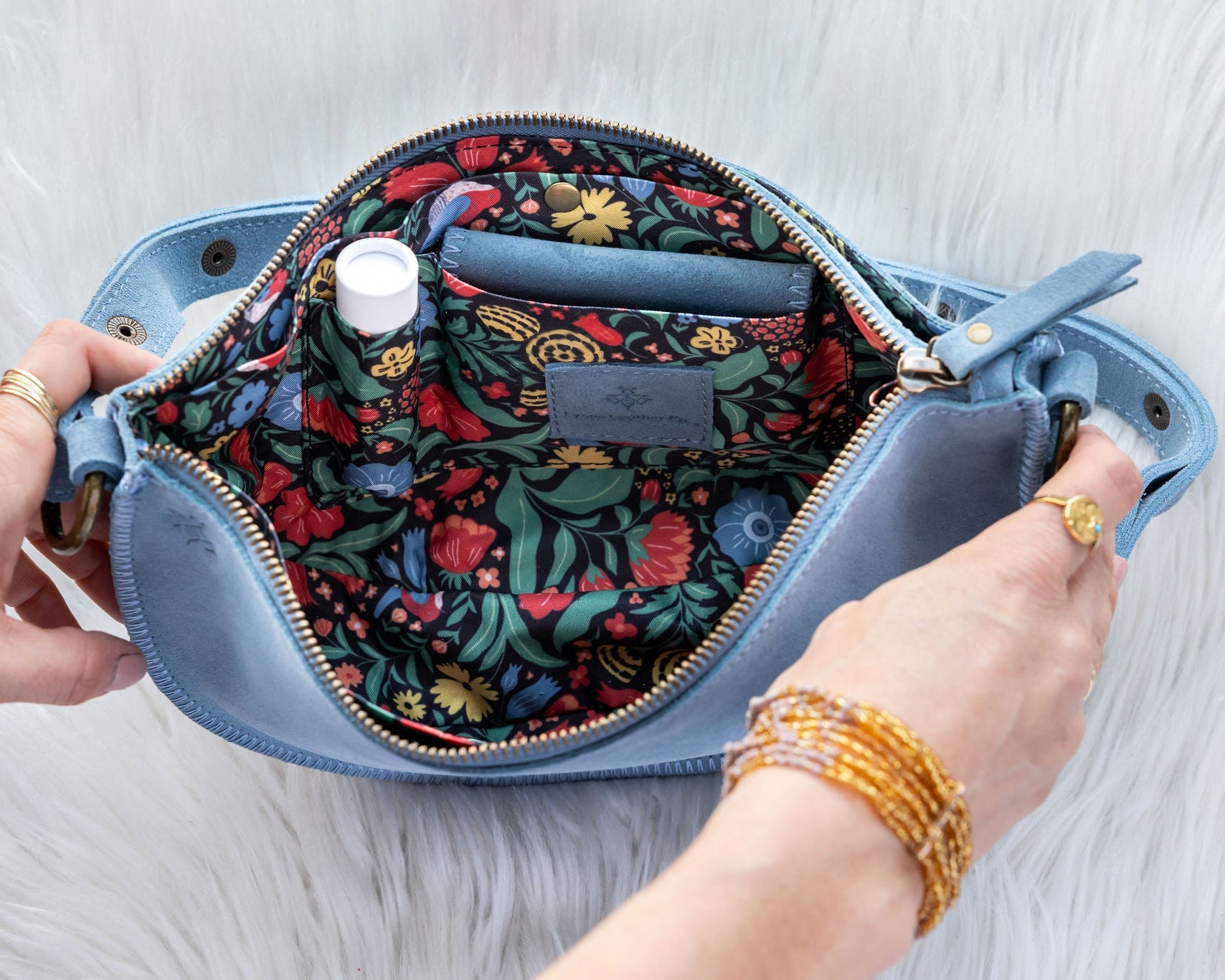 Blue handbag with floral interior, held open by hands on a light gray background