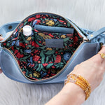 Blue handbag with floral interior, held open by hands on a light gray background