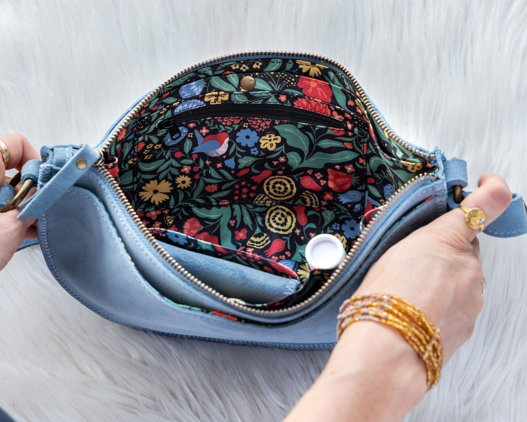 Hand holding a blue clutch with floral interior on a light wooden surface