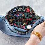 Hand holding a blue clutch with floral interior on a light wooden surface