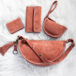 Set of mauve leather bags and wallets on a textured white surface