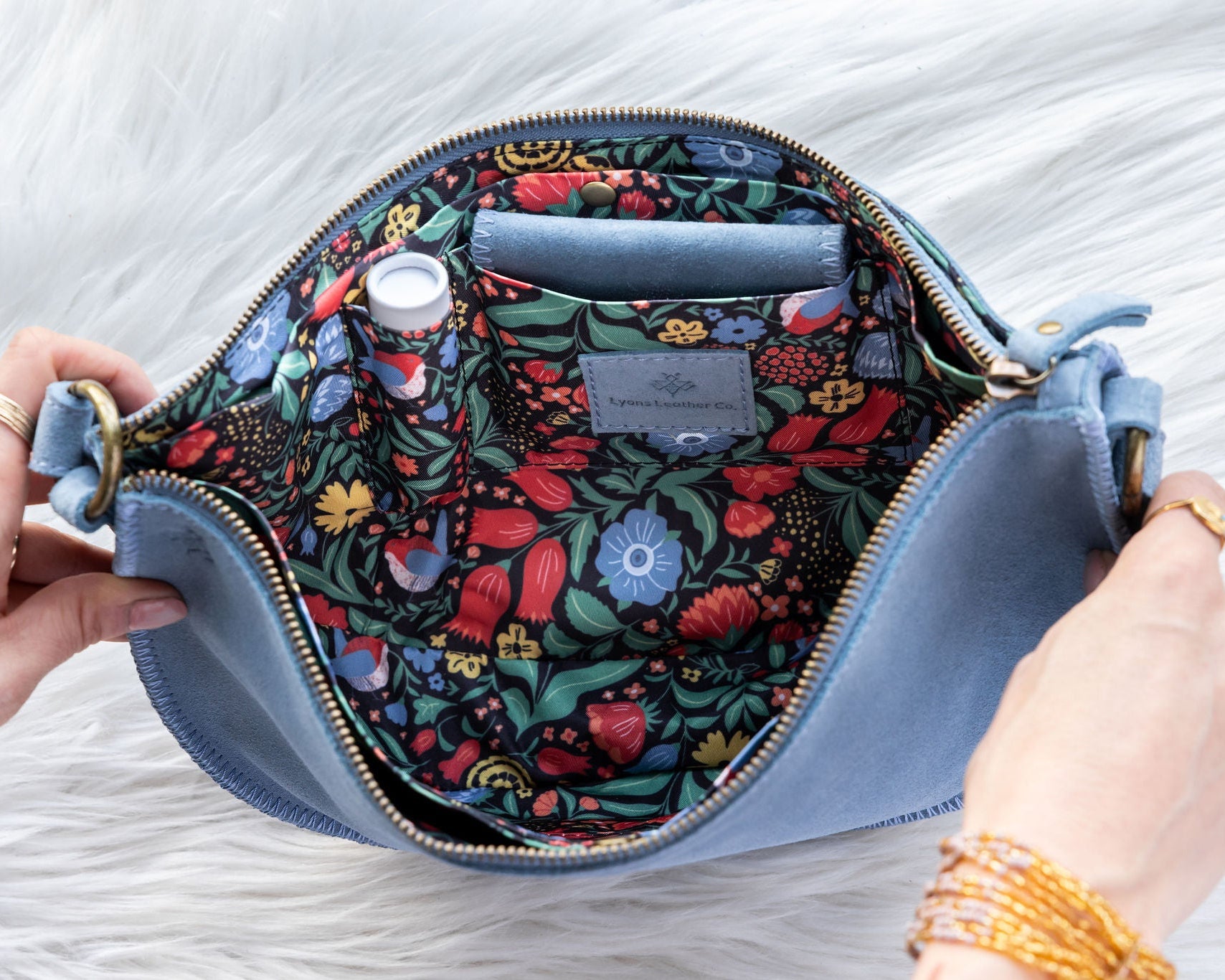 Floral-patterned bag with a blue exterior held by hands on a light background