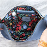 Floral-patterned bag with a blue exterior held by hands on a light background