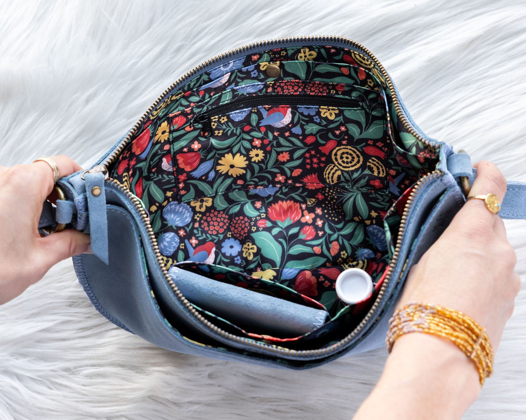 Floral-patterned pouch with a blue zipper held by hands on a white background