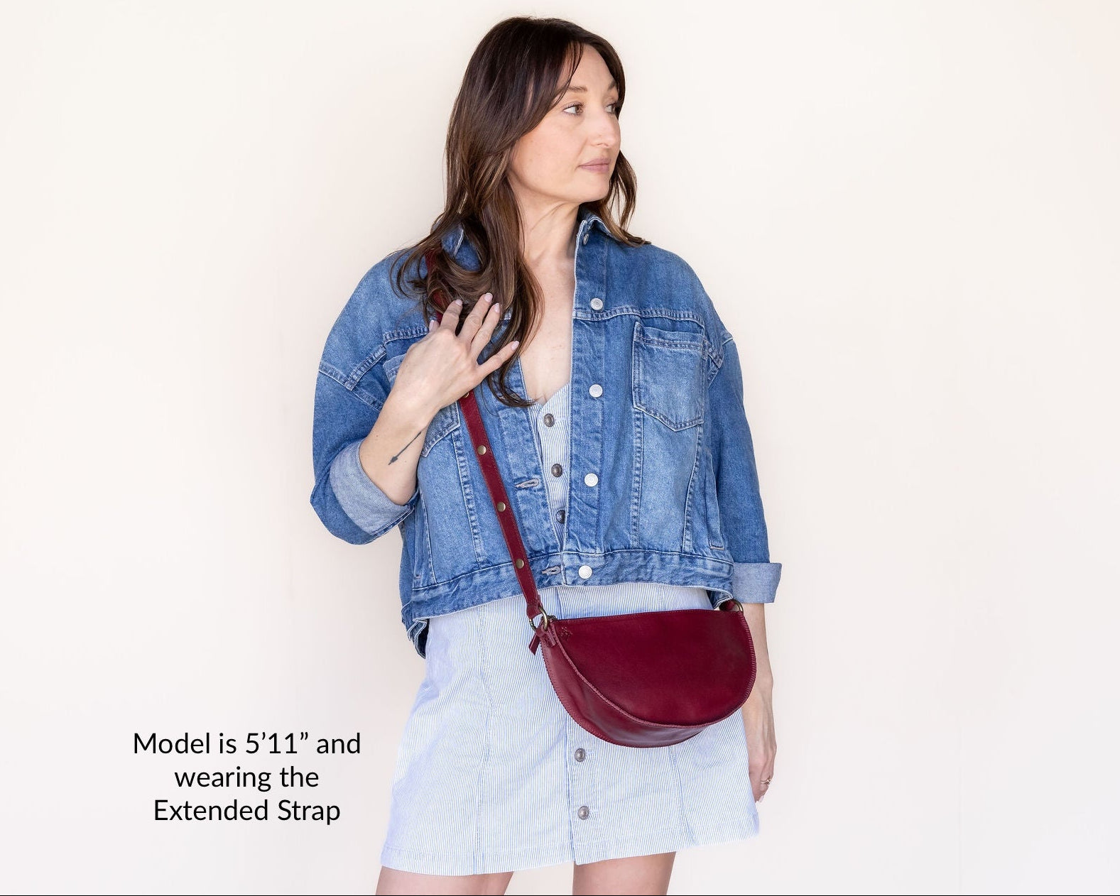 Woman wearing a denim jacket and holding a red handbag against a plain background