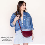 Woman wearing a denim jacket and holding a red handbag against a plain background