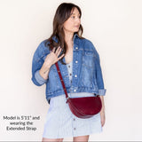 Woman wearing a denim jacket and holding a red handbag against a plain background