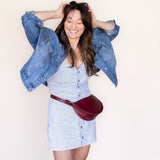 Woman wearing a denim jacket and white dress with a red bag against a plain background