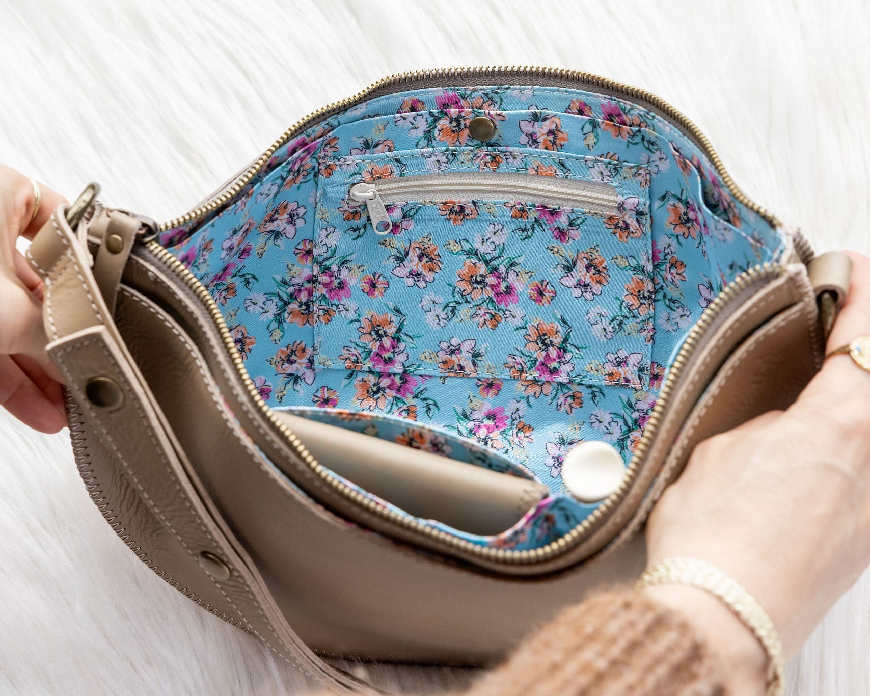Handbag with floral interior lining held by a person on a white background