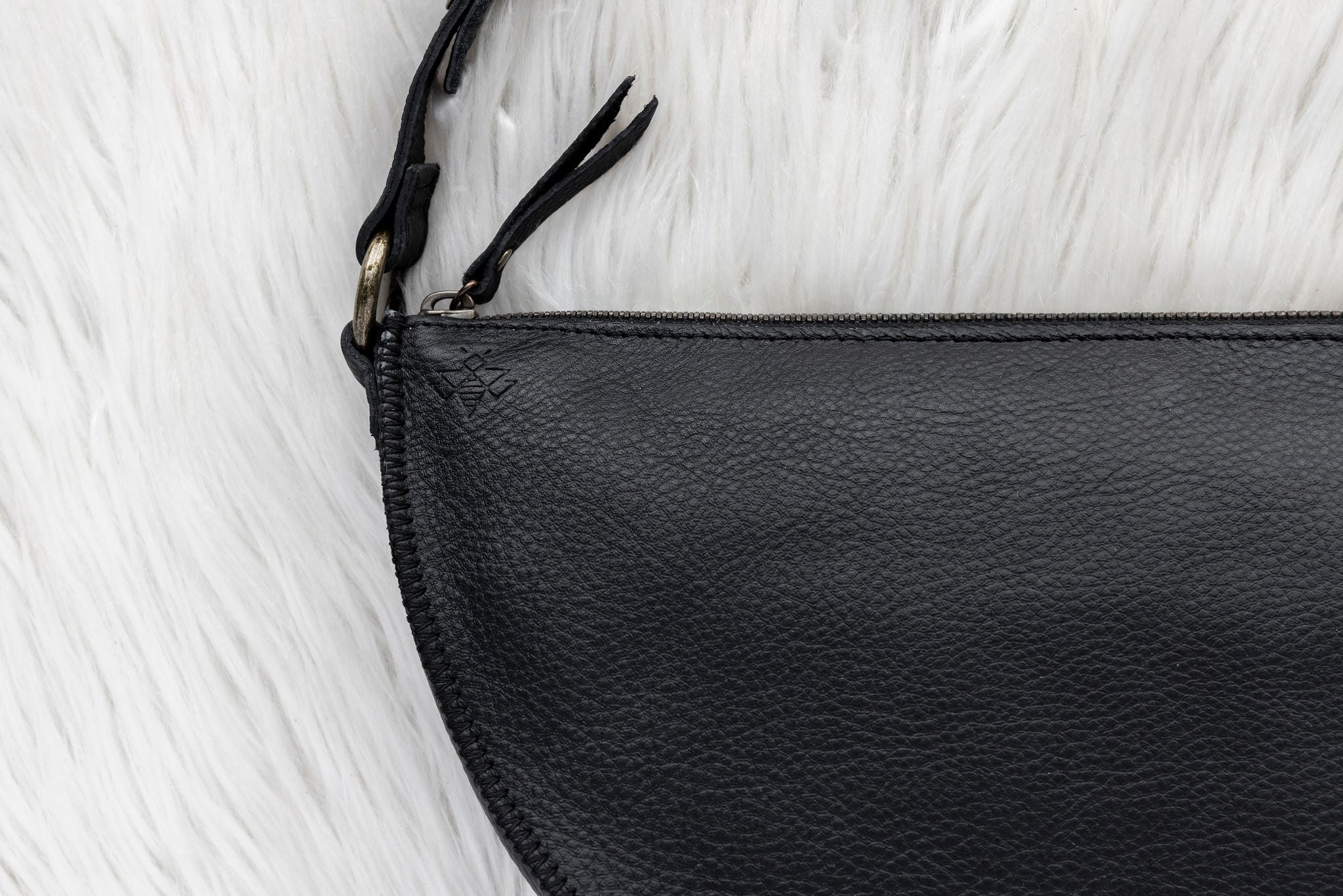 Close-up of a black leather pouch with a zipper on a white textured background