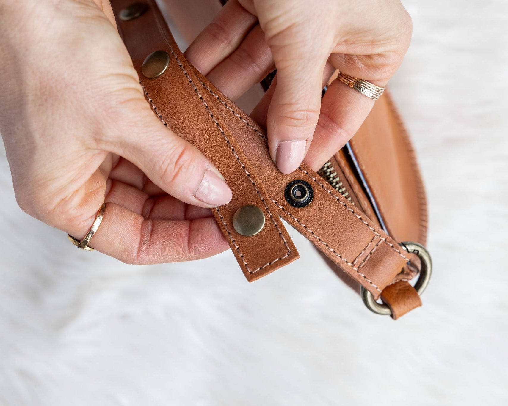 Close-up of hands holding a brown leather strap with metal hardware on a white background