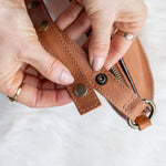 Close-up of hands holding a brown leather strap with metal hardware on a white background