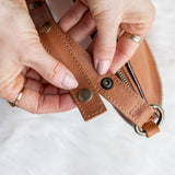 Close-up of hands holding a brown leather strap with metal hardware on a white background