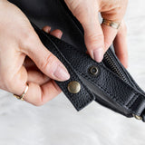 Close-up of hands holding a black leather wallet with visible buttons on a light background