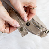 Close-up of hands holding a beige leather wallet on a light background