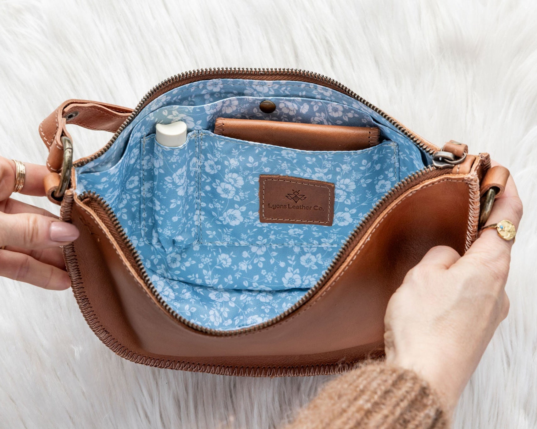 Brown leather handbag with blue interior and floral pattern, held open by a hand on a white background.