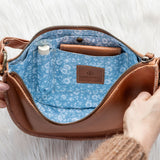 Brown leather handbag with blue interior and floral pattern, held open by a hand on a white background.