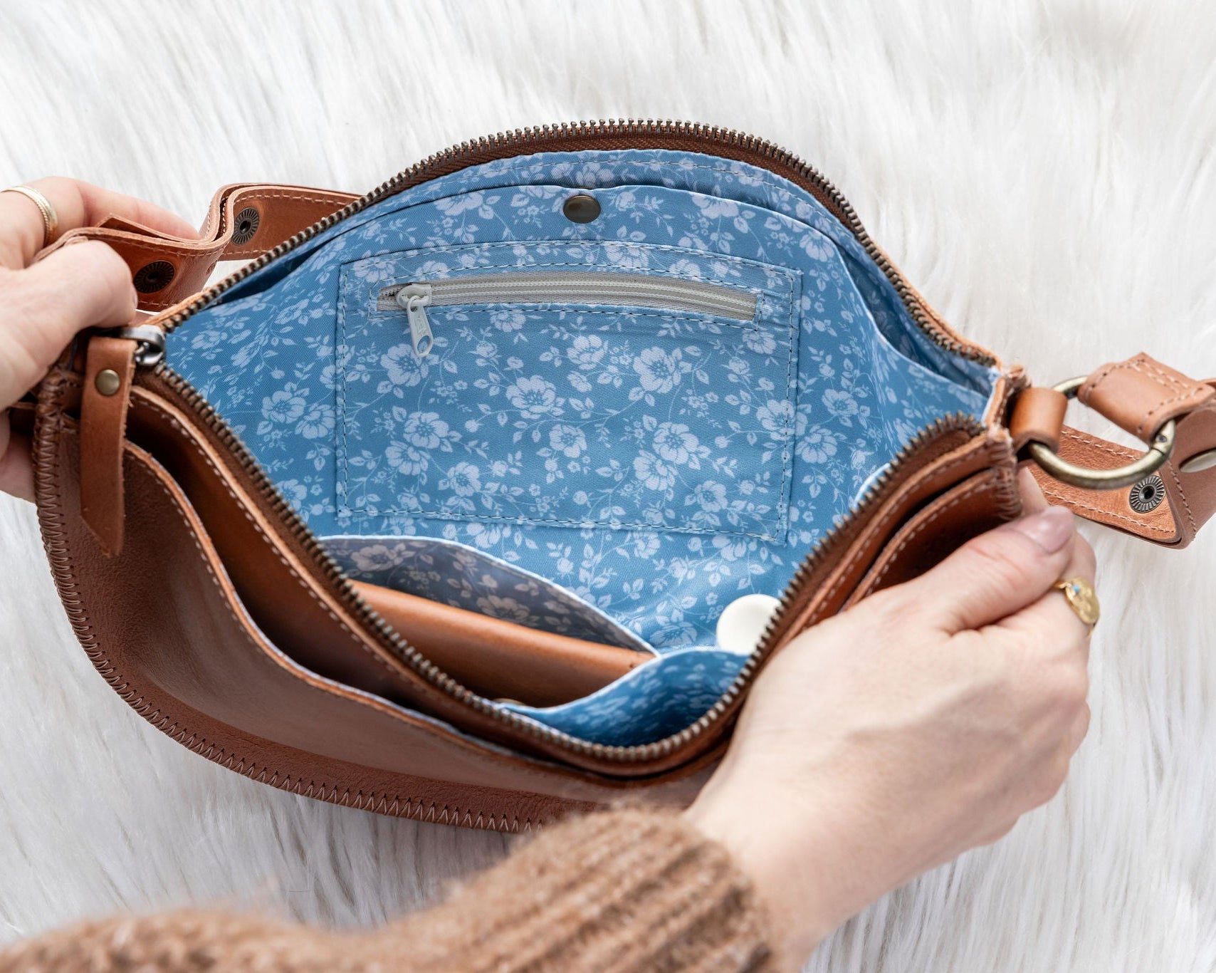 Brown leather bag with blue floral interior held by a person against a white background