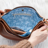 Brown leather bag with blue floral interior held by a person against a white background