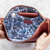 Handbag with floral interior lining held by a person on a white background