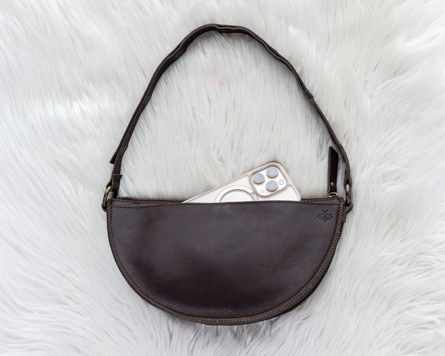 Brown leather bag with a phone inside on a white textured surface