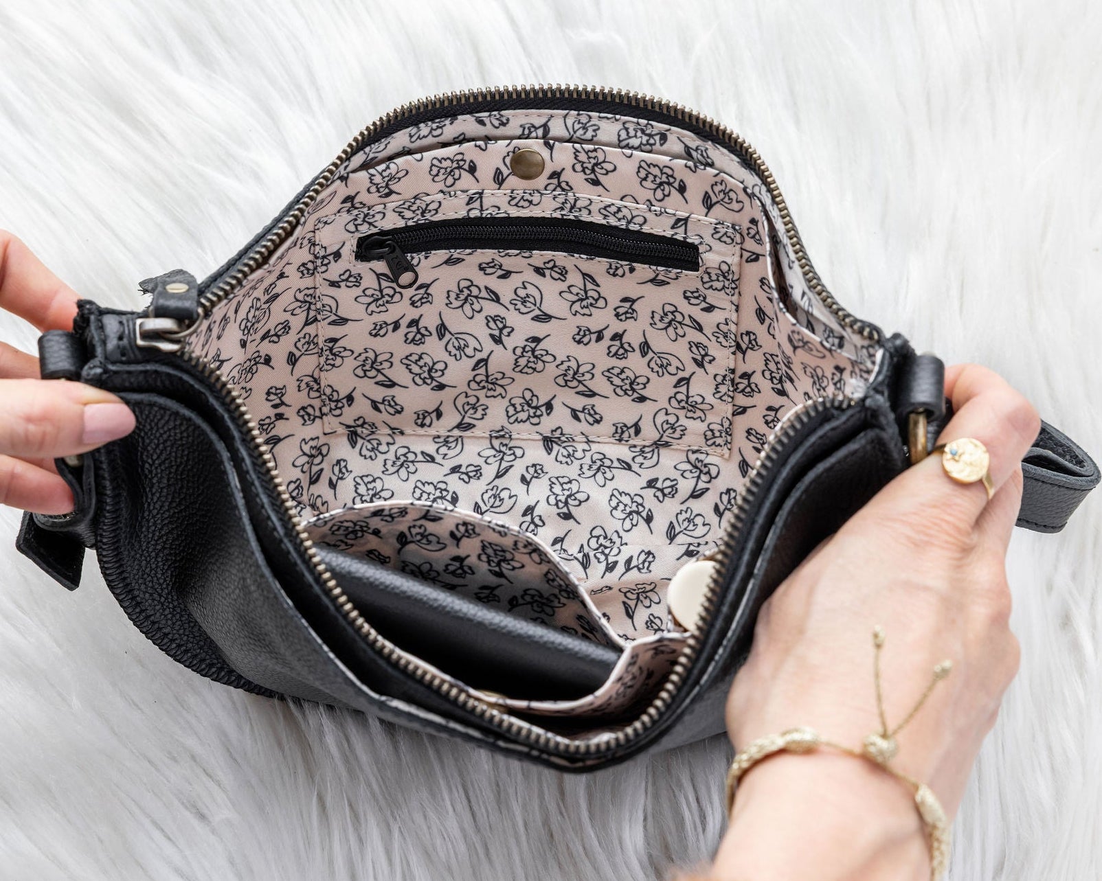 Black handbag with floral interior lining held by a person on a white background