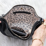Black handbag with floral interior lining held by a person on a white background